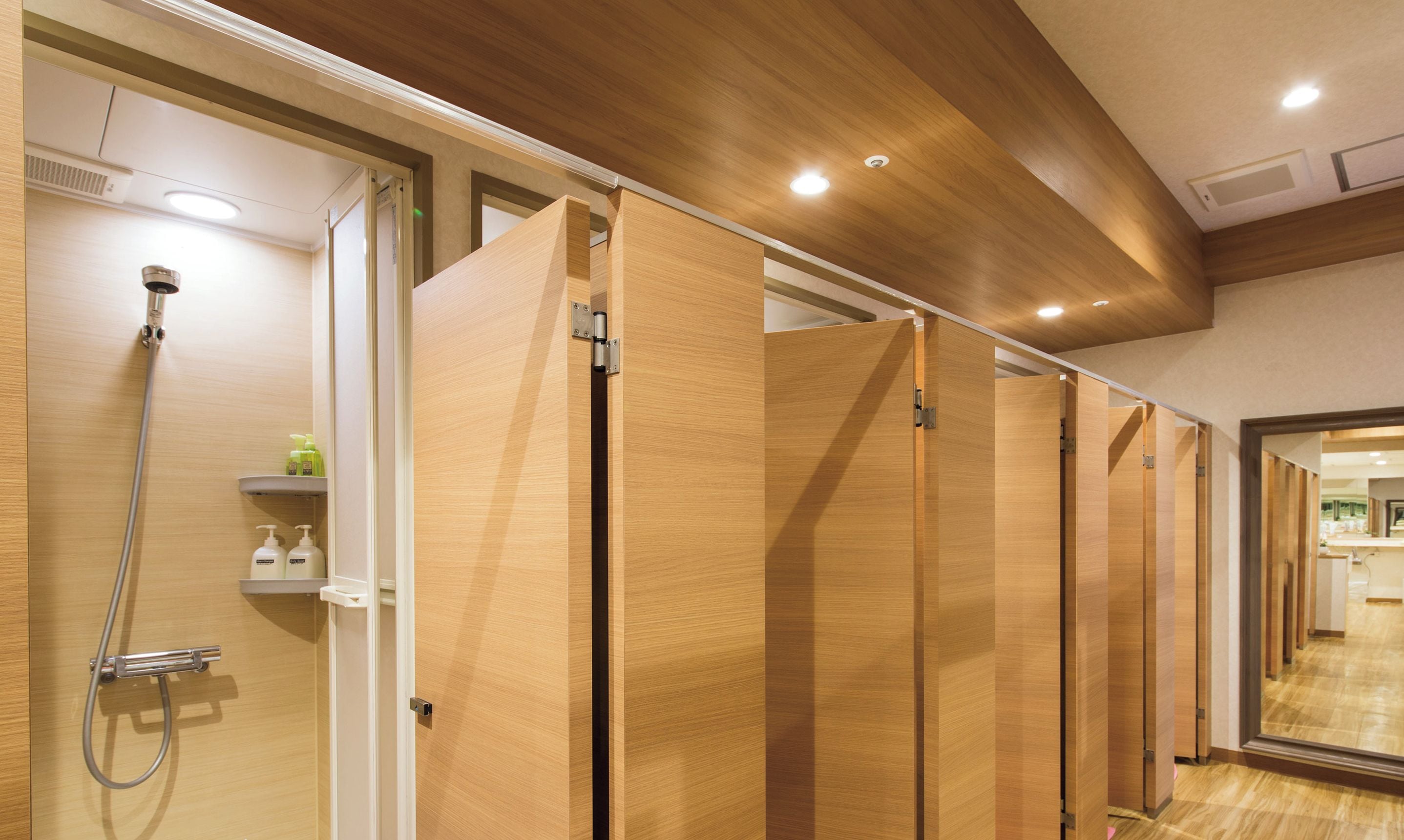 A hotel bathroom with wooden partitions, a shower area, and a mirror reflecting the interior.