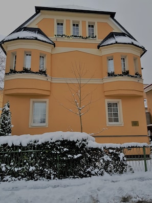 Um edifício de vários andares com fachada simétrica, grandes janelas e varandas cobertas de neve.