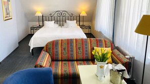 A hotel room with a bed, two bedside lamps, a sofa, a small table with a vase of flowers, and a radiator. - Apartment Barbara (Marianske Lazne)