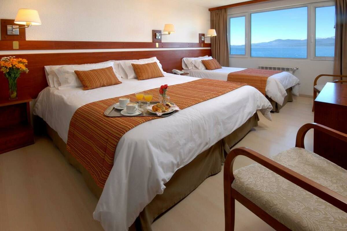 Habitación de hotel con dos camas, una mesa de comedor con desayuno y vista al mar.