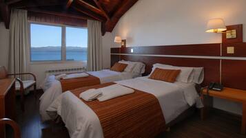 A hotel room with two beds, a desk, a chair, a nightstand with a phone, and a view of the sea.