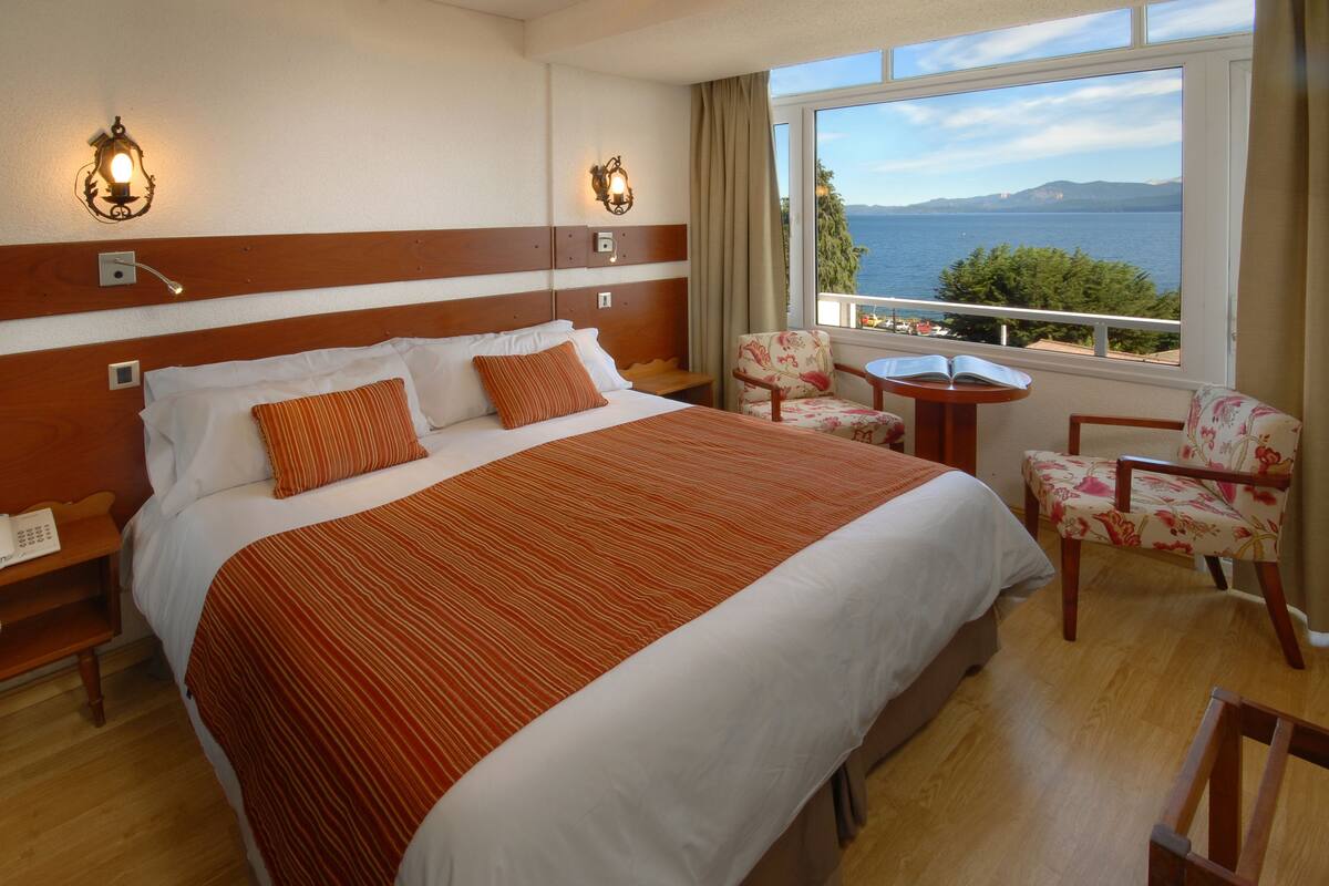 Habitación de hotel con una cama grande, dos sillas, una mesita y vista al mar.