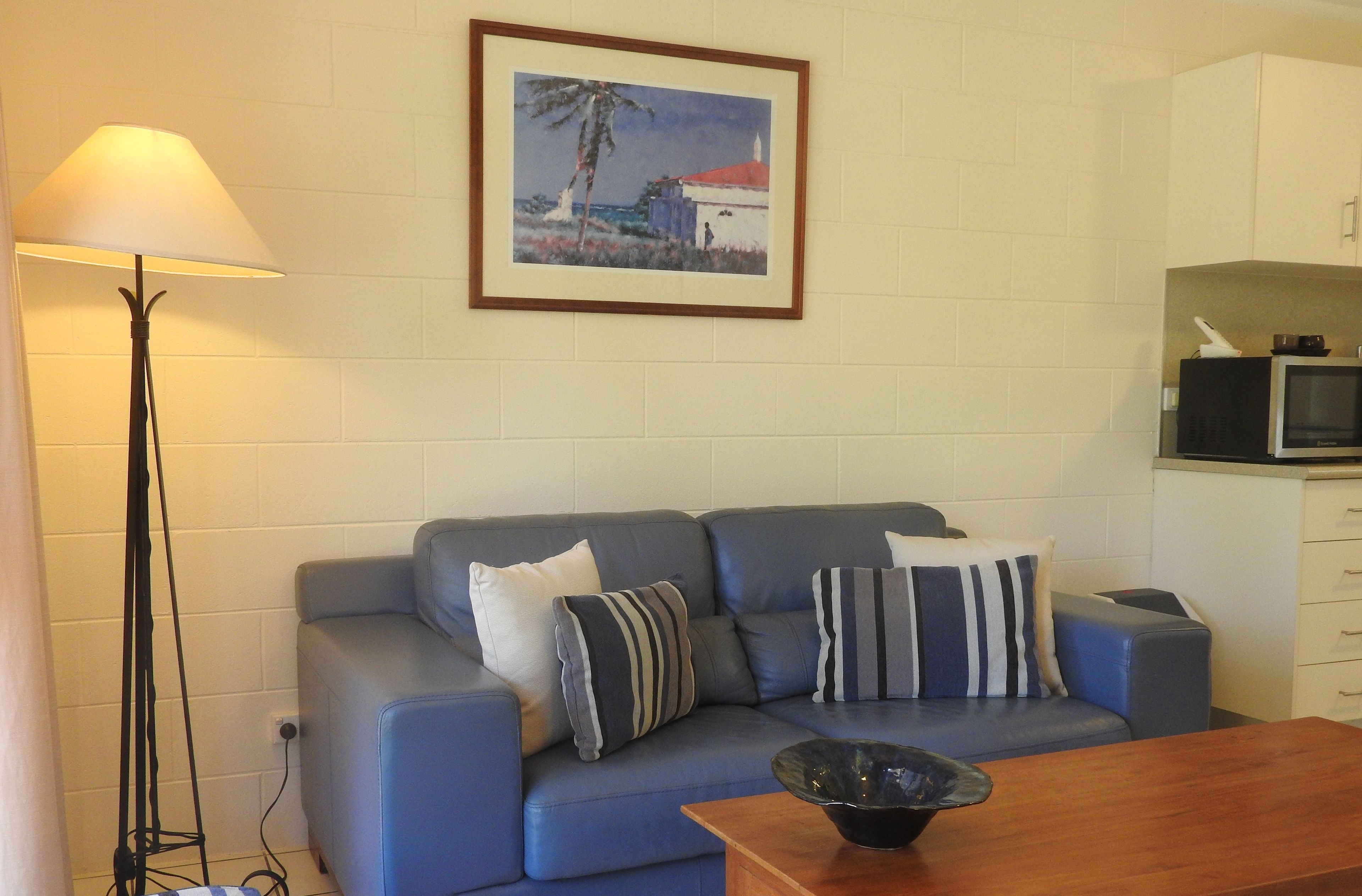 A living room with a blue sofa, striped pillows, a wooden coffee table, a floor lamp, and a framed painting on the wall.