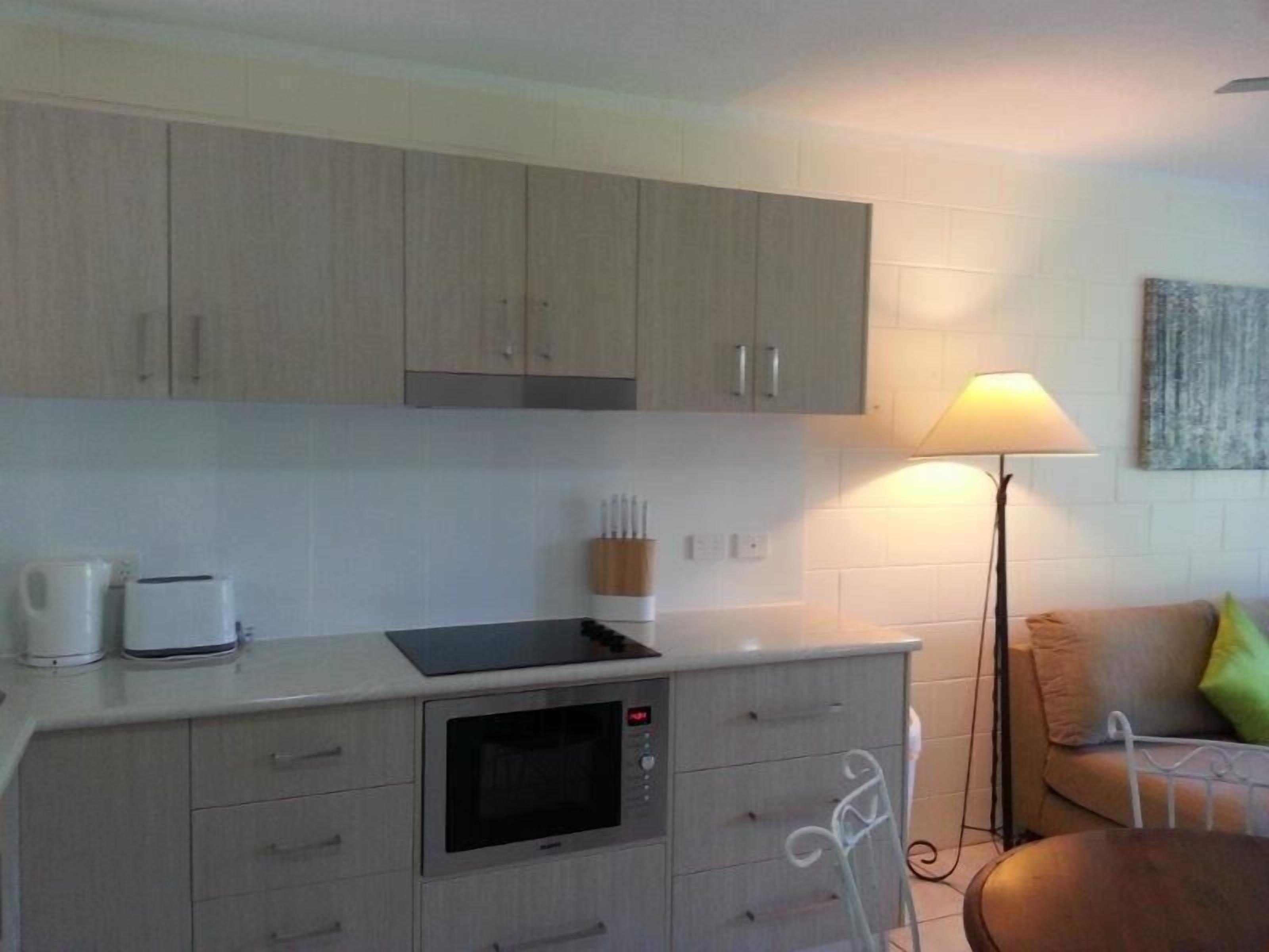 Eine kompakte Küche mit Einbauofen, Kaffeemaschine und Toaster. Im angrenzenden Wohnbereich steht eine weiße Lampe und ein Sofa mit Kissen.