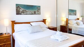 Una cama bien hecha con sábanas blancas, cabecera de madera y dos lámparas de noche.