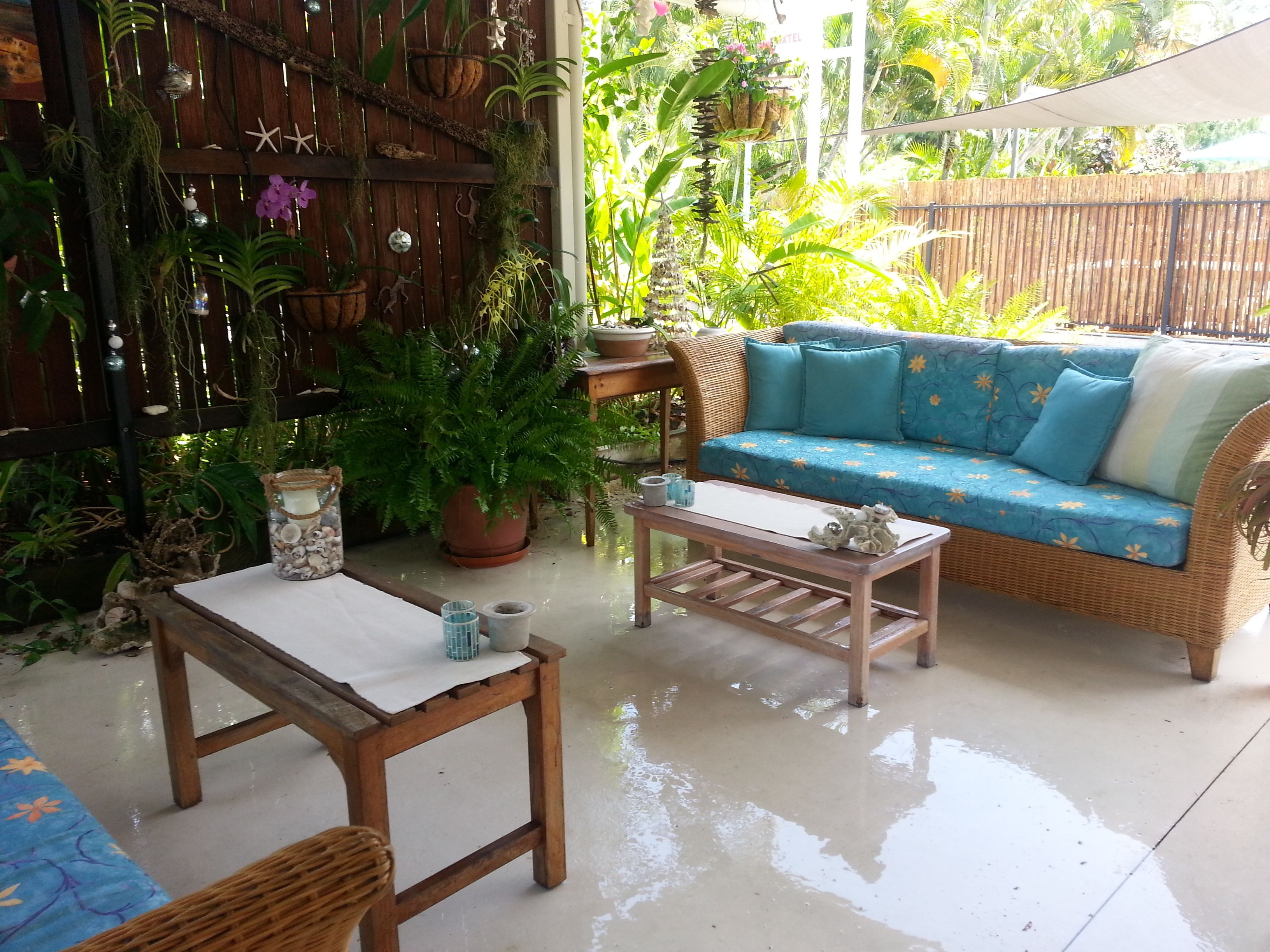 Un espacio al aire libre acogedor con un sofá de mimbre, una mesa de madera y varias macetas con plantas.