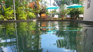Una piscina cristalina con reflejos de la vegetación circundante y un área de descanso con sombrillas.