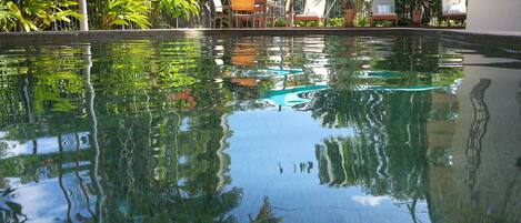 Piscina límpida com reflexos do verde ao redor e área de estar com guarda-sóis.