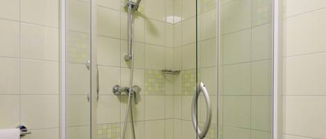 Ducha con mampara de vidrio, puerta blanca con manija, paredes con azulejos y piso blanco.