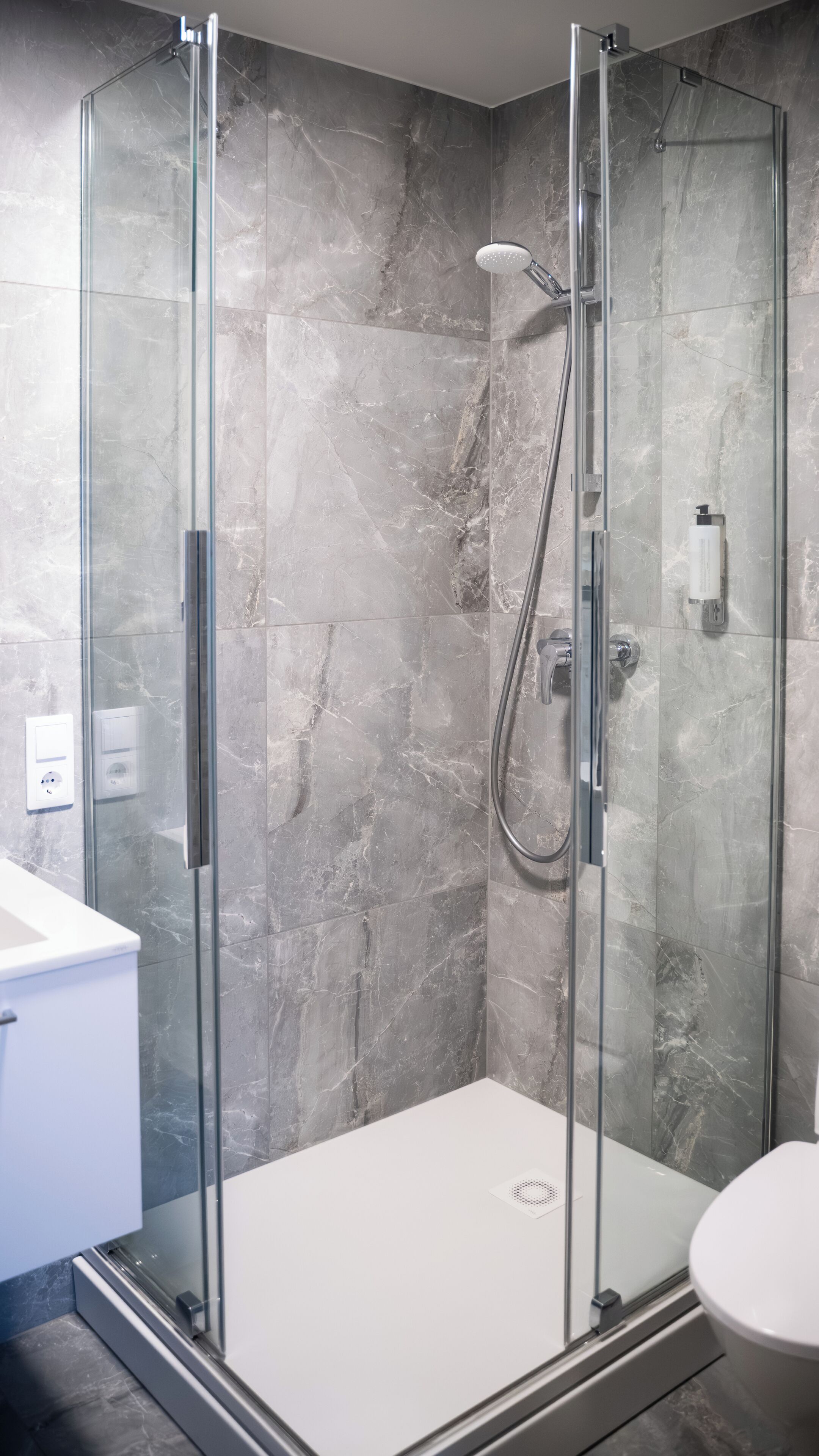 Une salle de bain moderne avec une douche à parois de verre, des murs en marbre et un lavabo blanc.