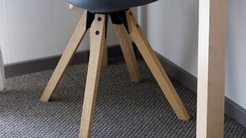 Uma cadeira com encosto curvo e pernas de madeira, colocada em uma mesa de canto com uma pequena planta.