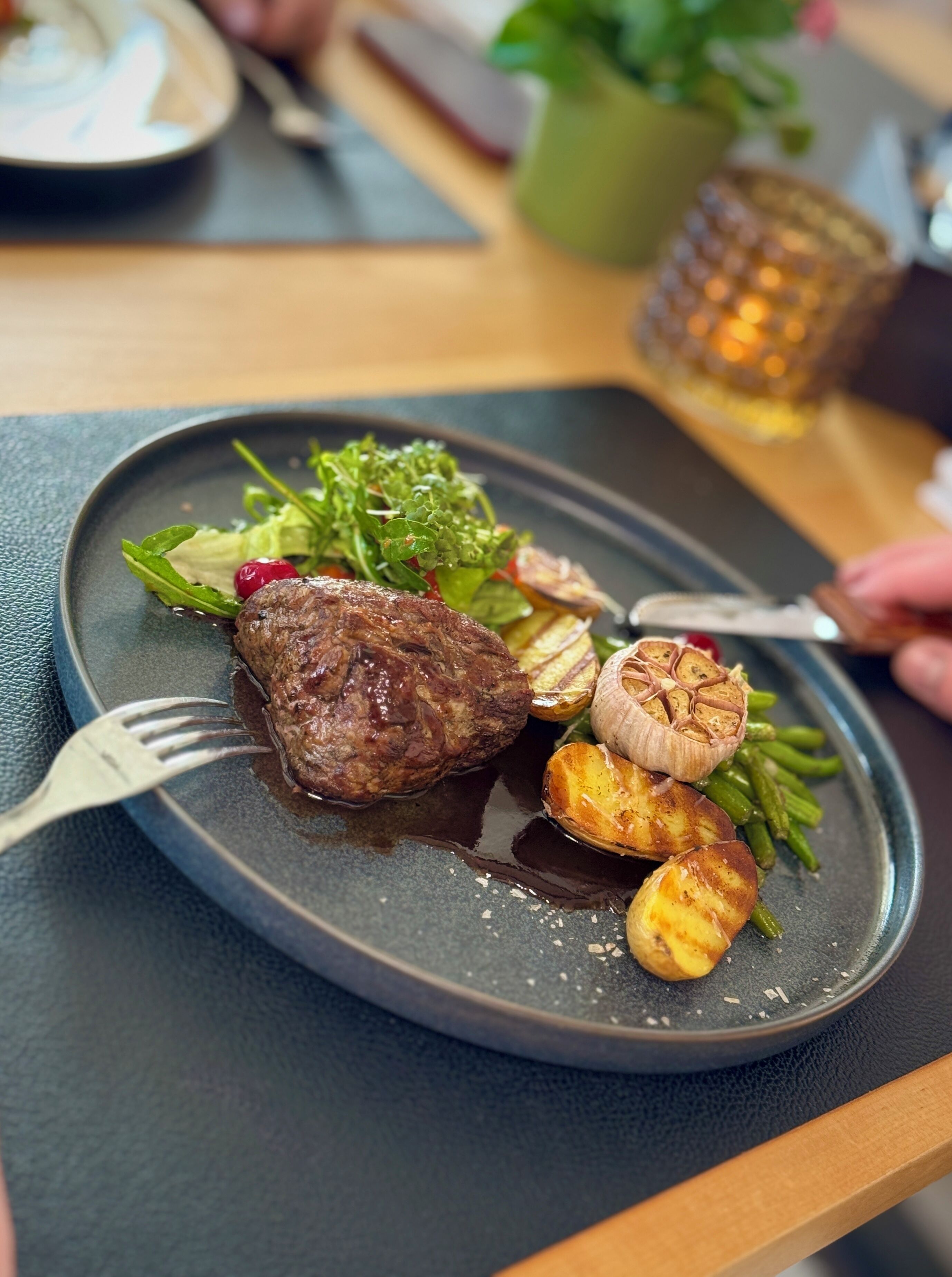 Um prato com bife, batatas assadas e vegetais sobre um prato escuro.