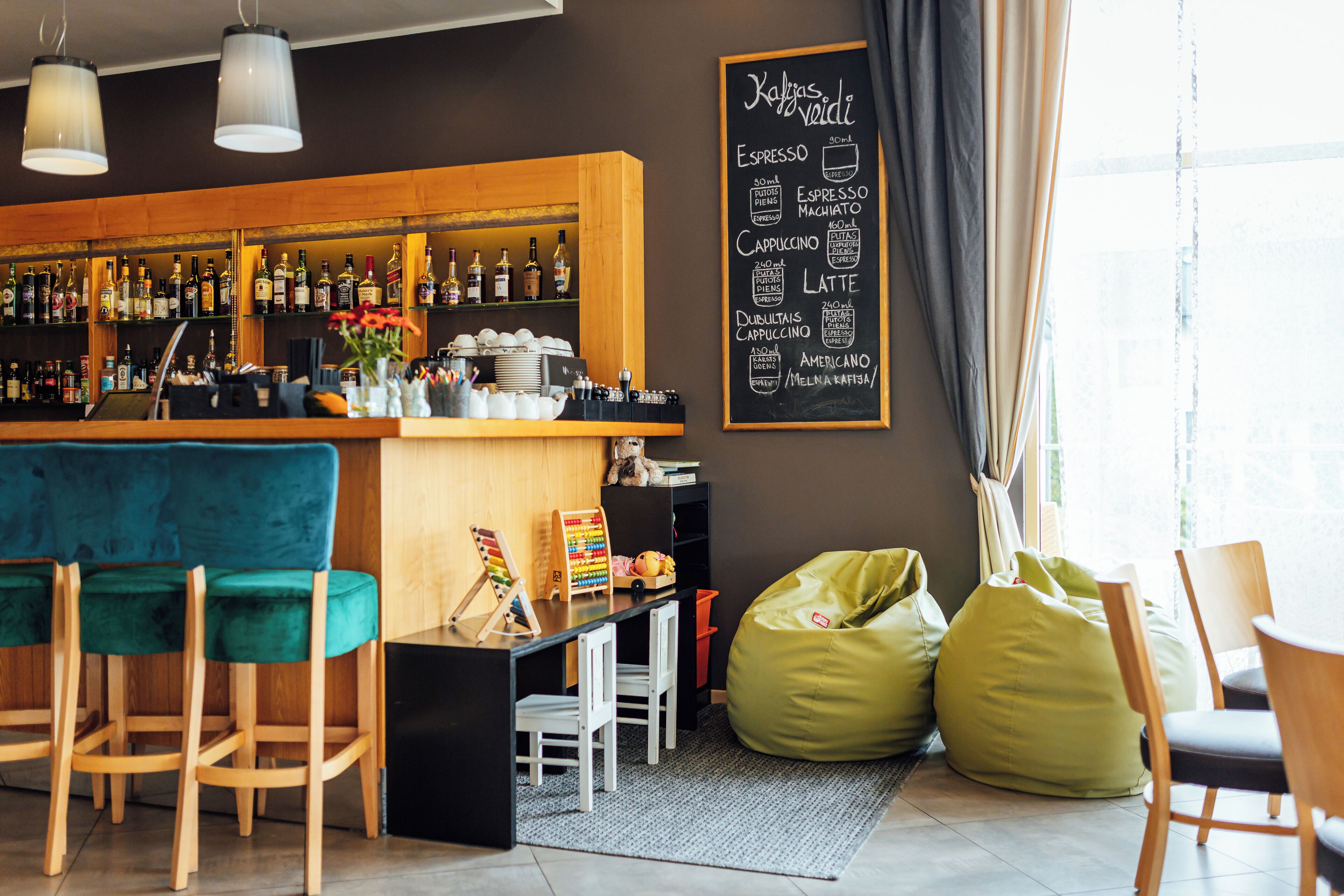 A bar area with a chalkboard menu, wooden bar counter, and seating with green and white chairs.