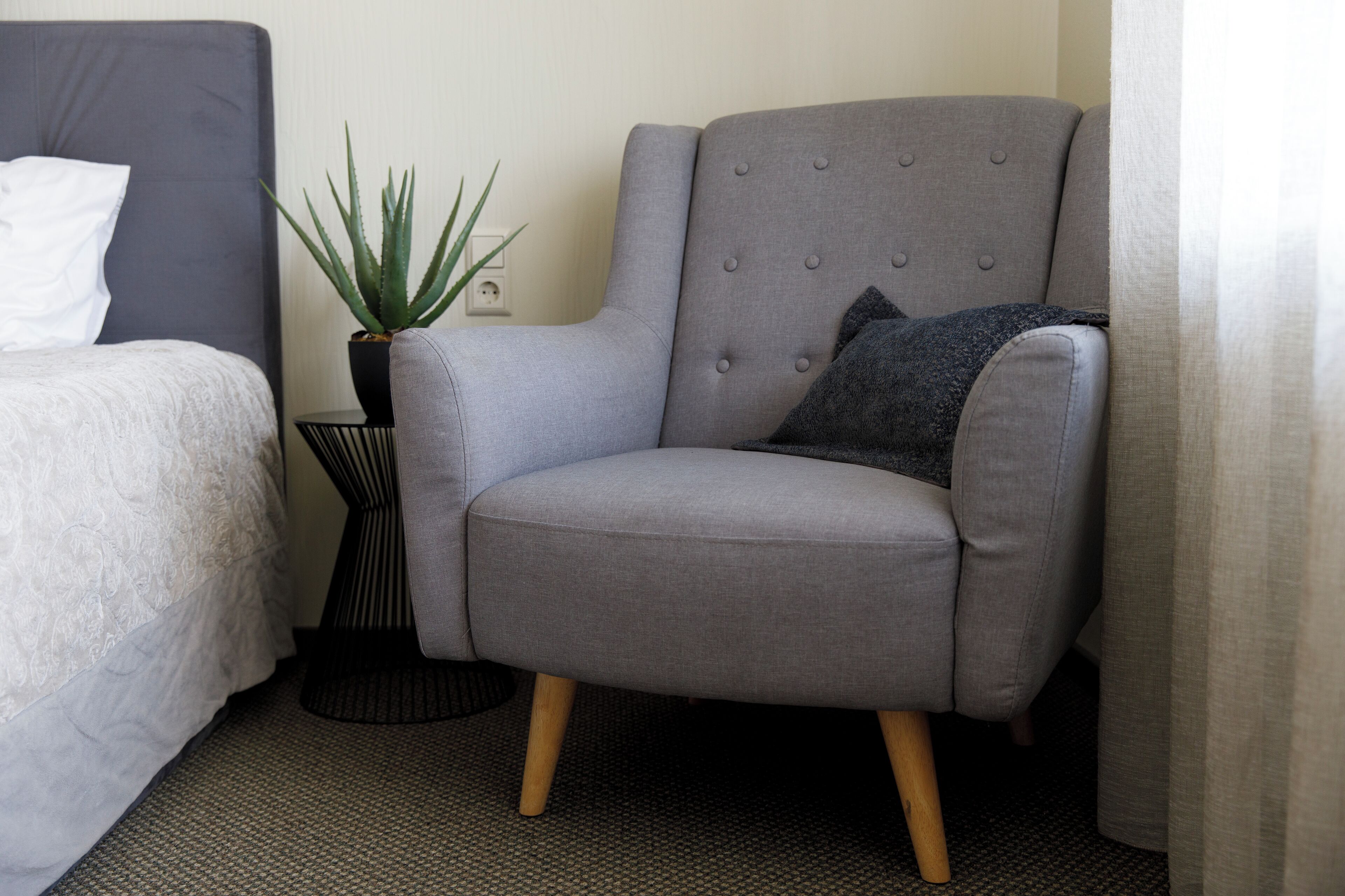 A grey armchair with wooden legs, a small potted plant, and a grey cushion.