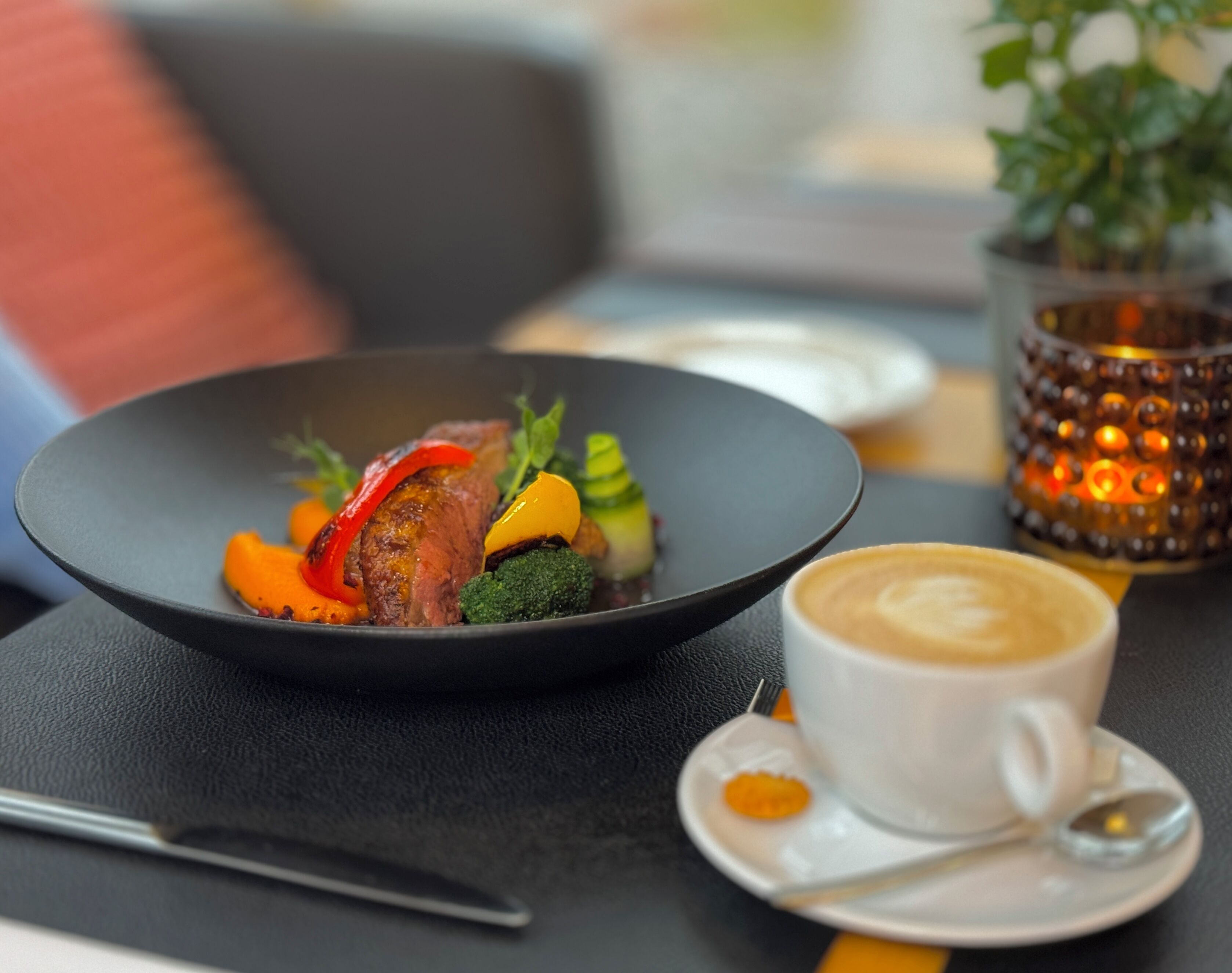 A plate of food with vegetables and meat, a cup of coffee, and a candle on a table.