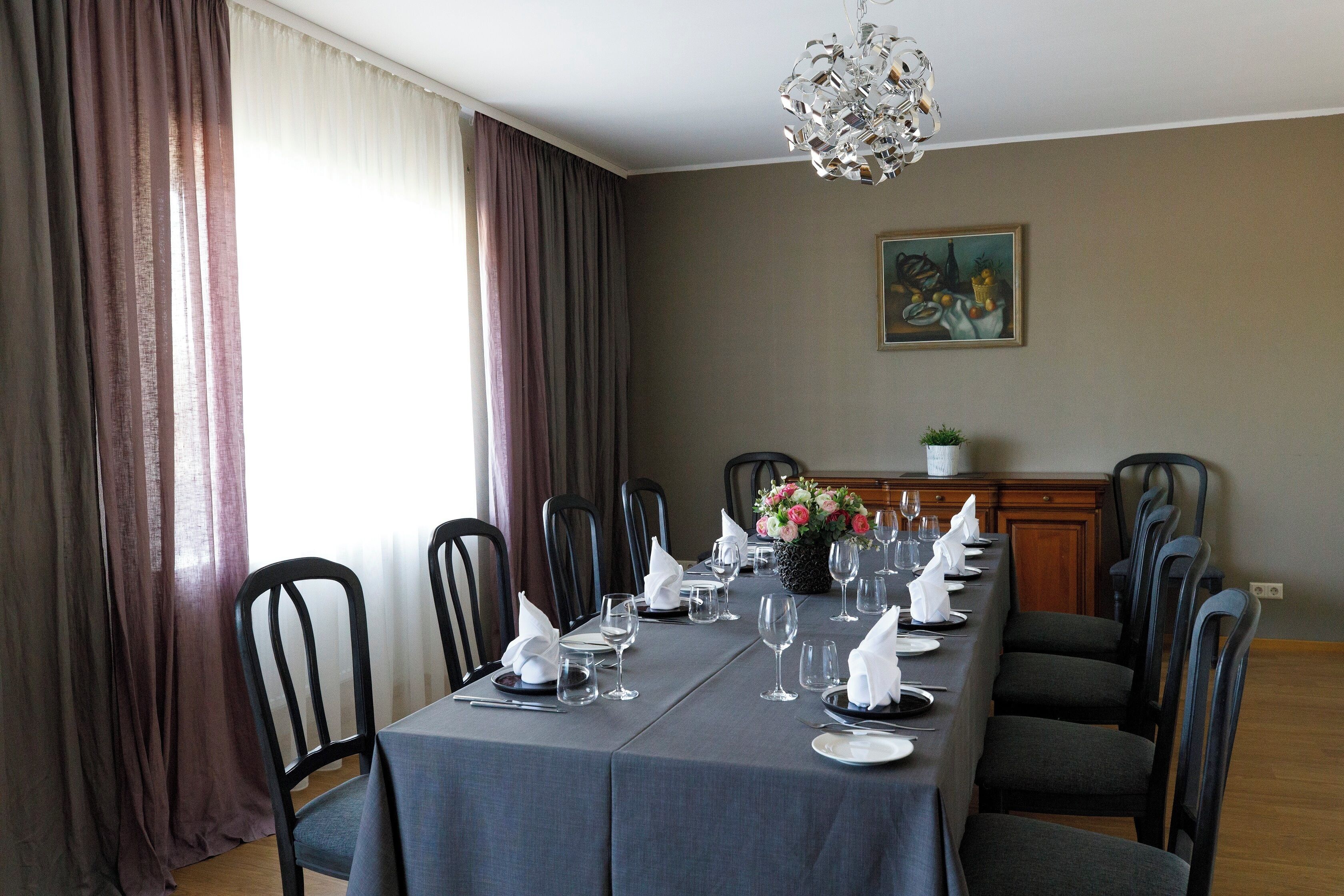 Una sala da pranzo con un lungo tavolo apparecchiato, sedie, un lampadario e un quadro appeso al muro.