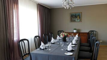 A dining room with a long table set for a meal, chairs, a chandelier, and a painting on the wall.