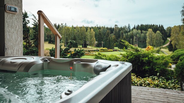 Una vasca idromassaggio con un pontile in legno e vista su un giardino curato e una foresta.