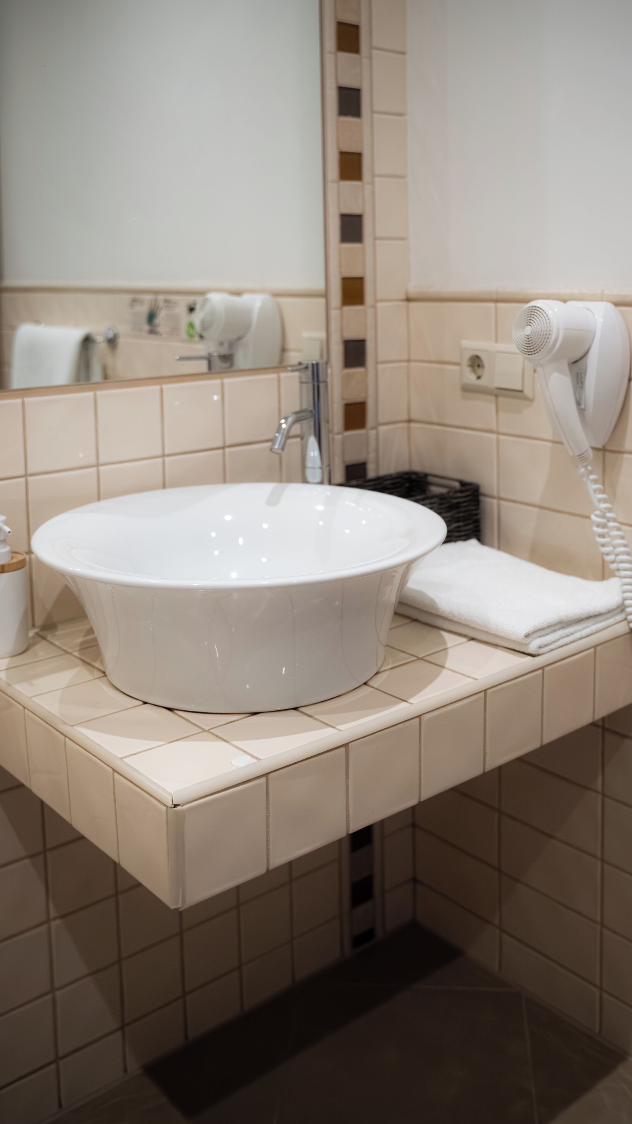 A bathroom with a white sink, a mirror, a hairdryer, and a towel on the counter.