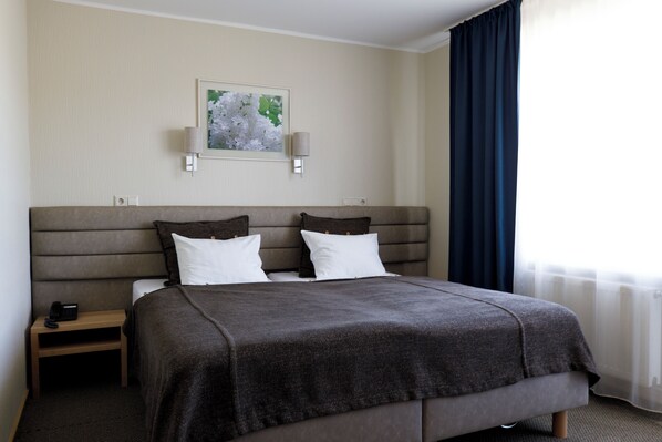 Habitación de hotel con una cama grande, dos mesitas de noche, una lámpara de pared y una ventana con cortinas.