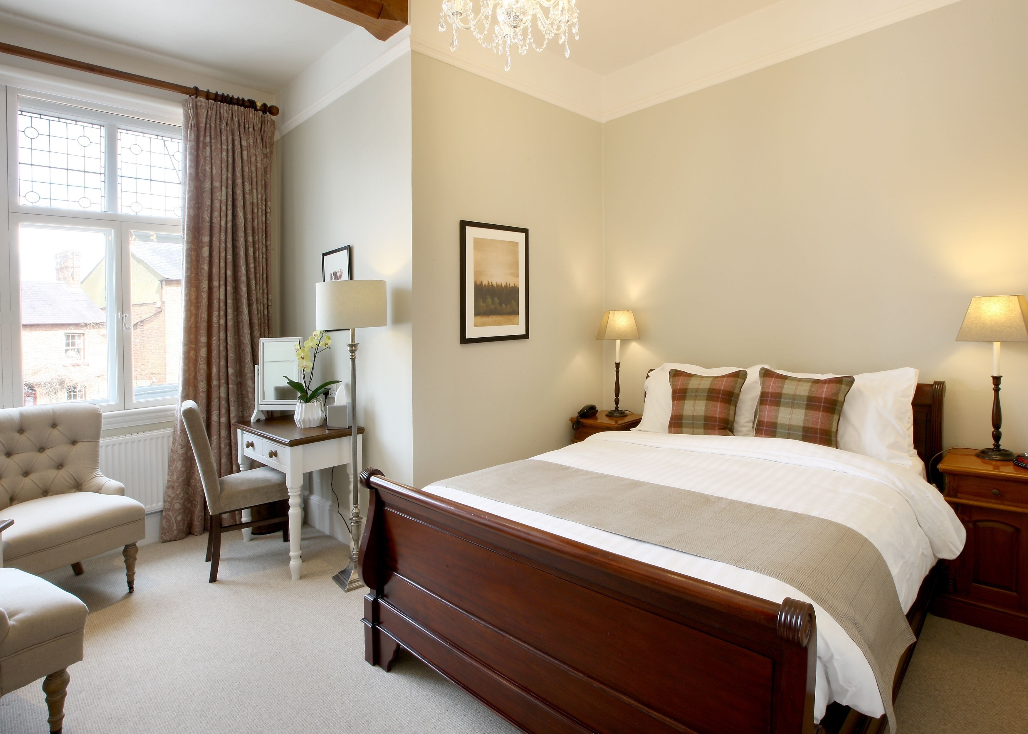 Hotelkamer met een groot bed, een bureau met lamp, een stoel en uitzicht door een raam.