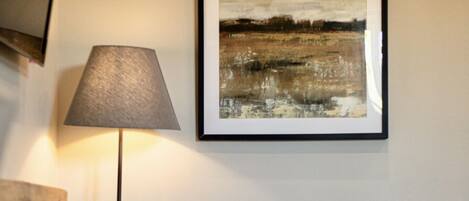 A tufted leather armchair, a floor lamp, and a framed abstract painting on a plain wall.