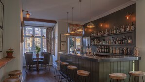 A bar area with wooden stools, a bar counter, and shelves with bottles. - The Five Arrows Hotel (Aylesbury)