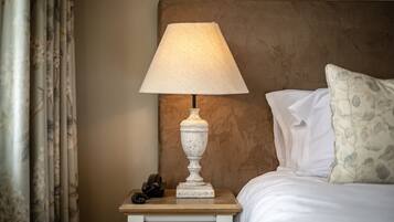Een net opgemaakt bed met witte lakens, een decoratieve lamp op een nachtkastje en een kussen met bloemenprint.
