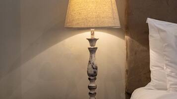 A bedside table with a lamp, a clock, and a framed botanical print on the wall.