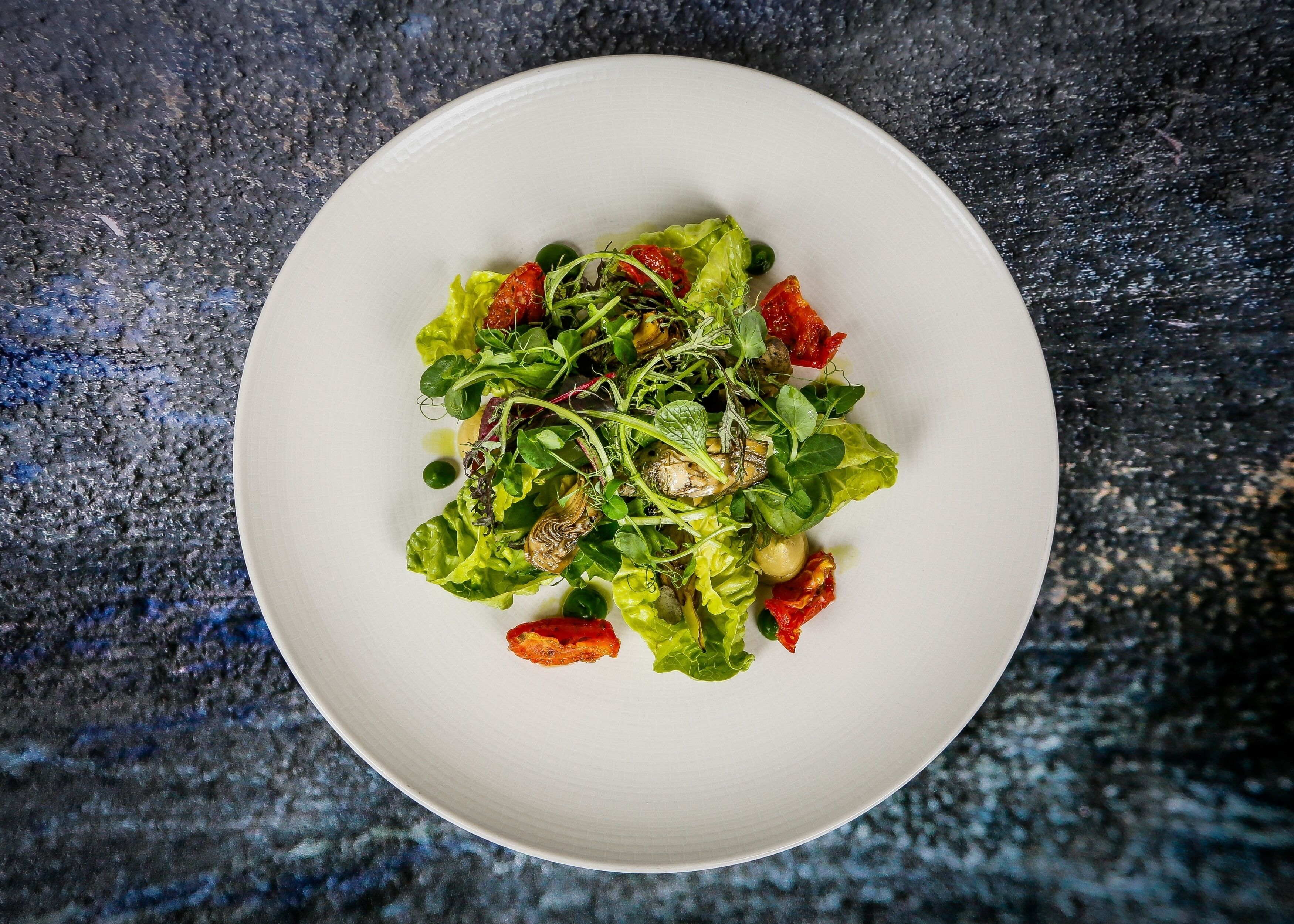 Un plato blanco con una ensalada sobre una superficie oscura y con textura.