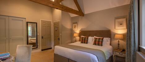 A bedroom with a large bed, wooden beams, a chair, bedside tables, and a window with curtains.