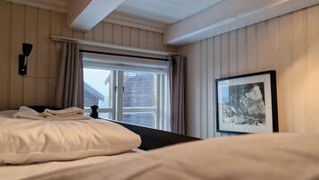 A bedroom with a bed, a window with curtains, a wall-mounted light, and a framed picture.