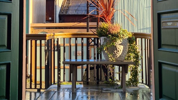 An outdoor patio with a table and chairs, a railing, and potted plants. - Vertshuset Røros (Roros)
