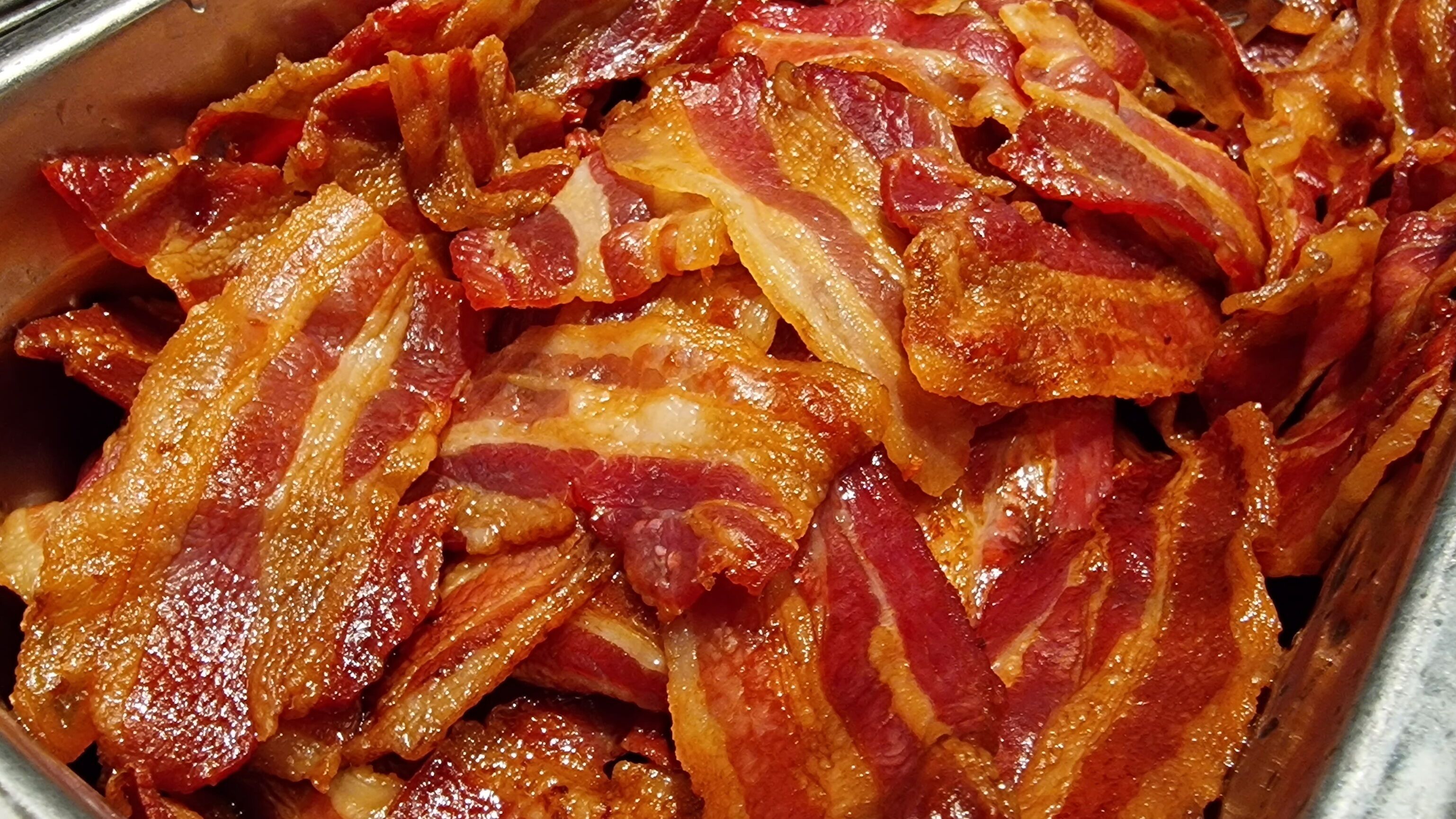 A metal container filled with cooked bacon strips.
