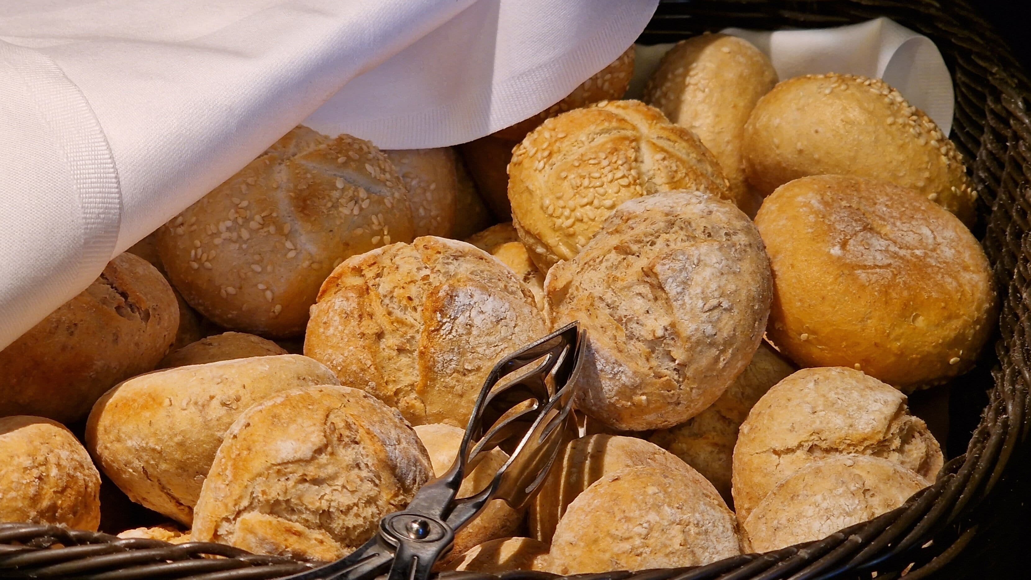 A basket filled with various types of bread, including rolls and baguettes.
