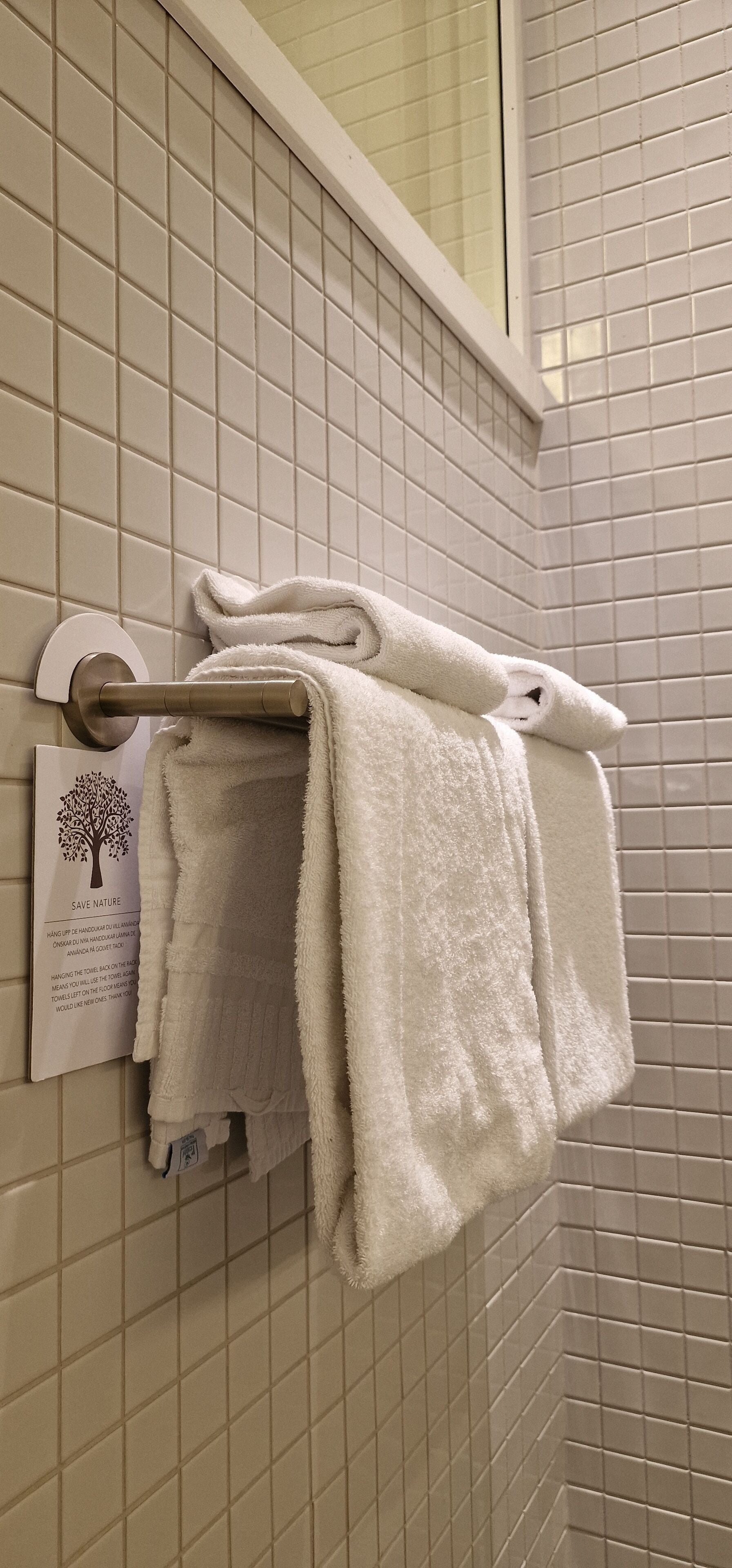 A bathroom with beige tiled walls and a towel rack holding two white towels.