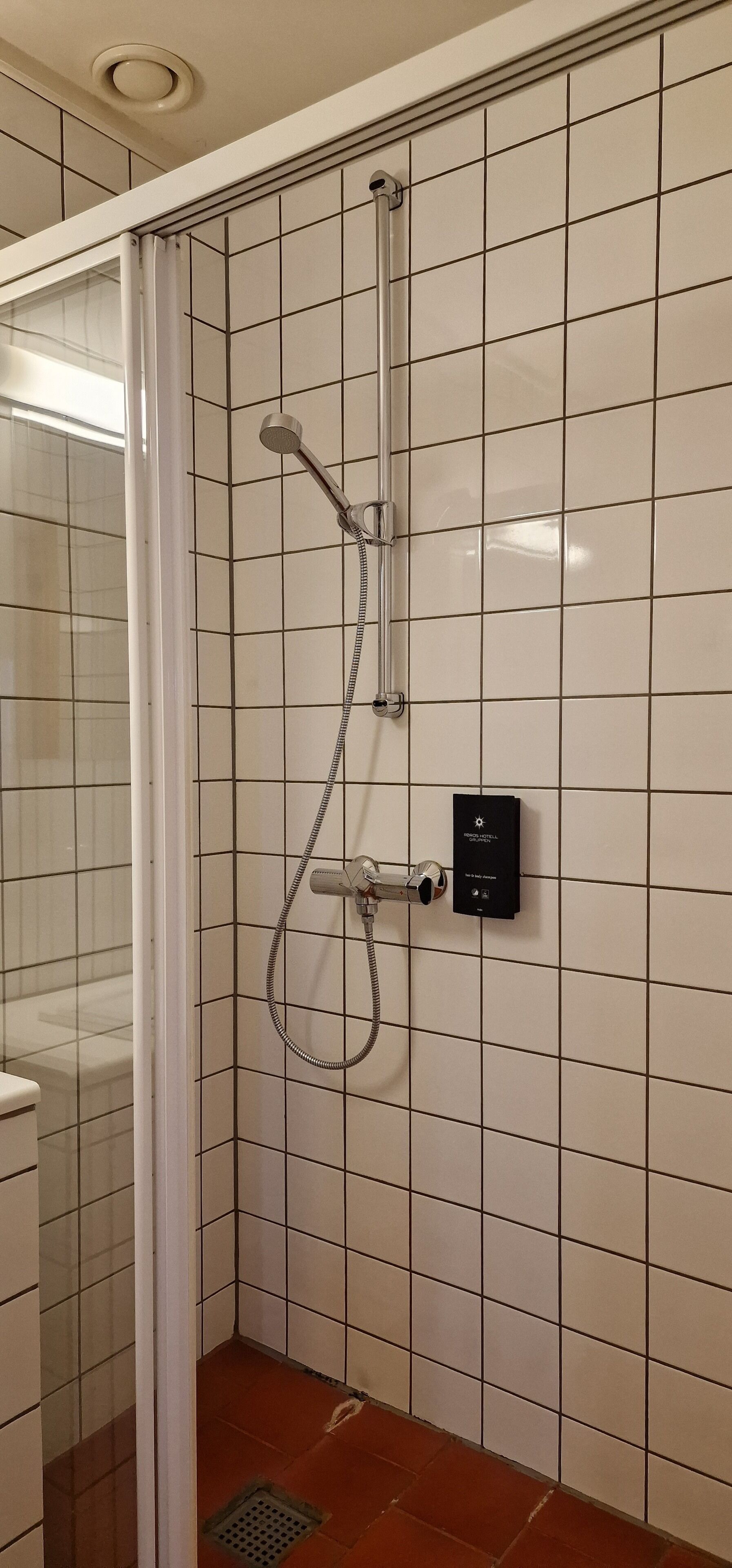 A shower with a handheld showerhead and a wall-mounted control panel.