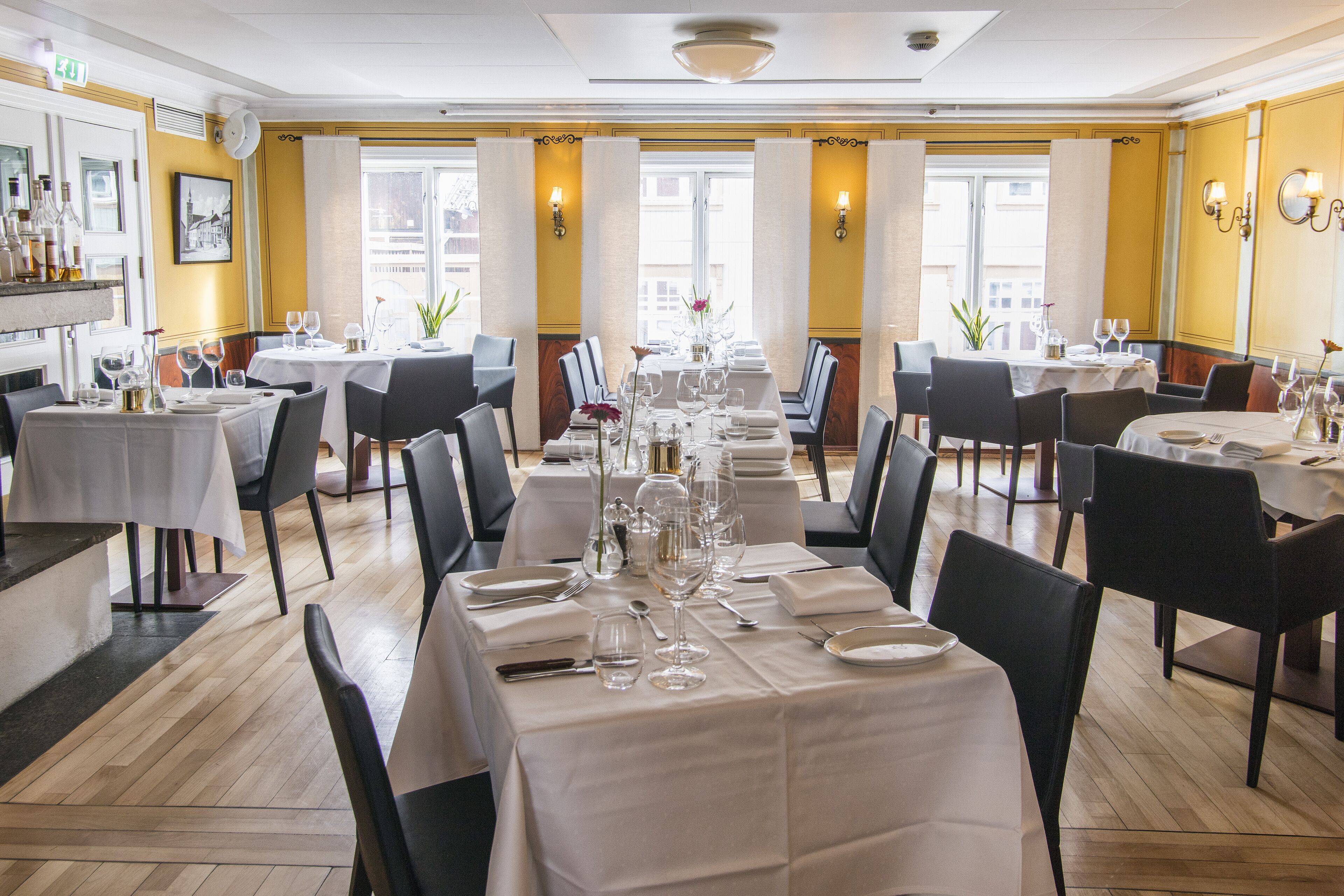 A restaurant with multiple tables set for dining, featuring white tablecloths and chairs.