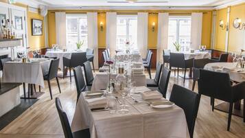 A restaurant with multiple tables set for dining, featuring white tablecloths and chairs.