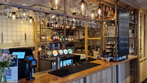 A bar area with a cash register, beer taps, and shelves stocked with bottles and glasses. - Vertshuset Røros (Roros)