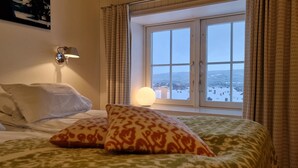 A hotel room with a bed, pillows, a bedside lamp, and a window with curtains. - Vertshuset Røros (Roros)