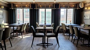 A restaurant with multiple tables and chairs, large windows with curtains, and hanging pendant lights. - Vertshuset Røros (Roros)
