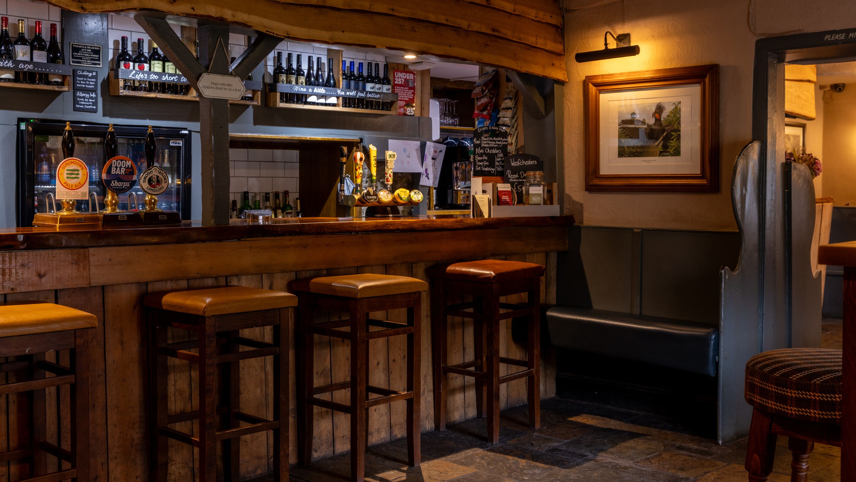 A bar area with wooden stools, a variety of beer taps, and a framed picture on the wall.