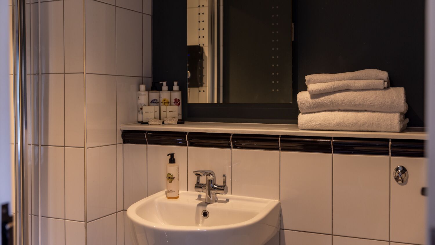 A bathroom with a white sink, a mirror, and a shelf with toiletries and towels.