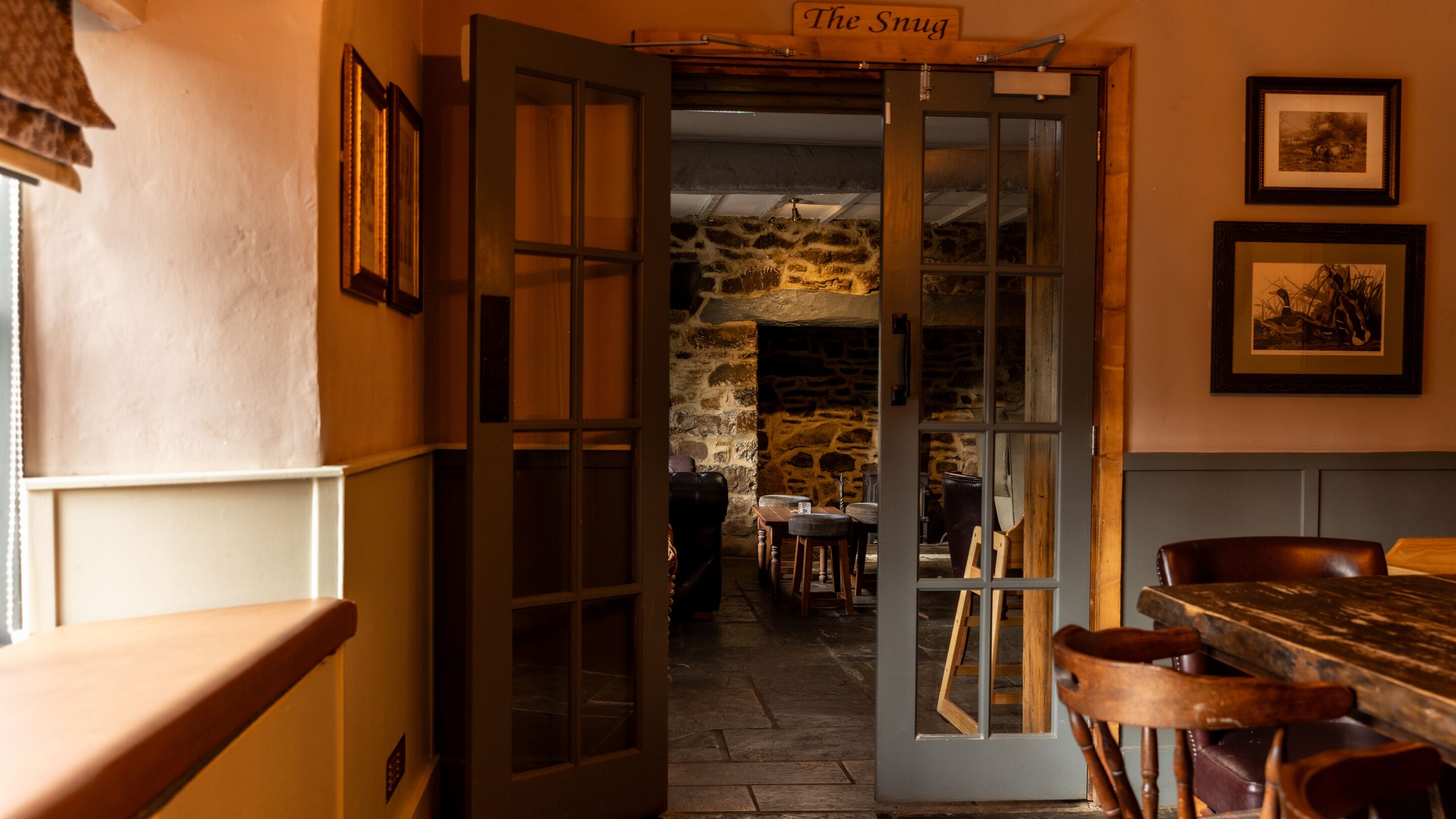 An interior with a stone wall, wooden furniture, and a sign reading 'The Snug'.