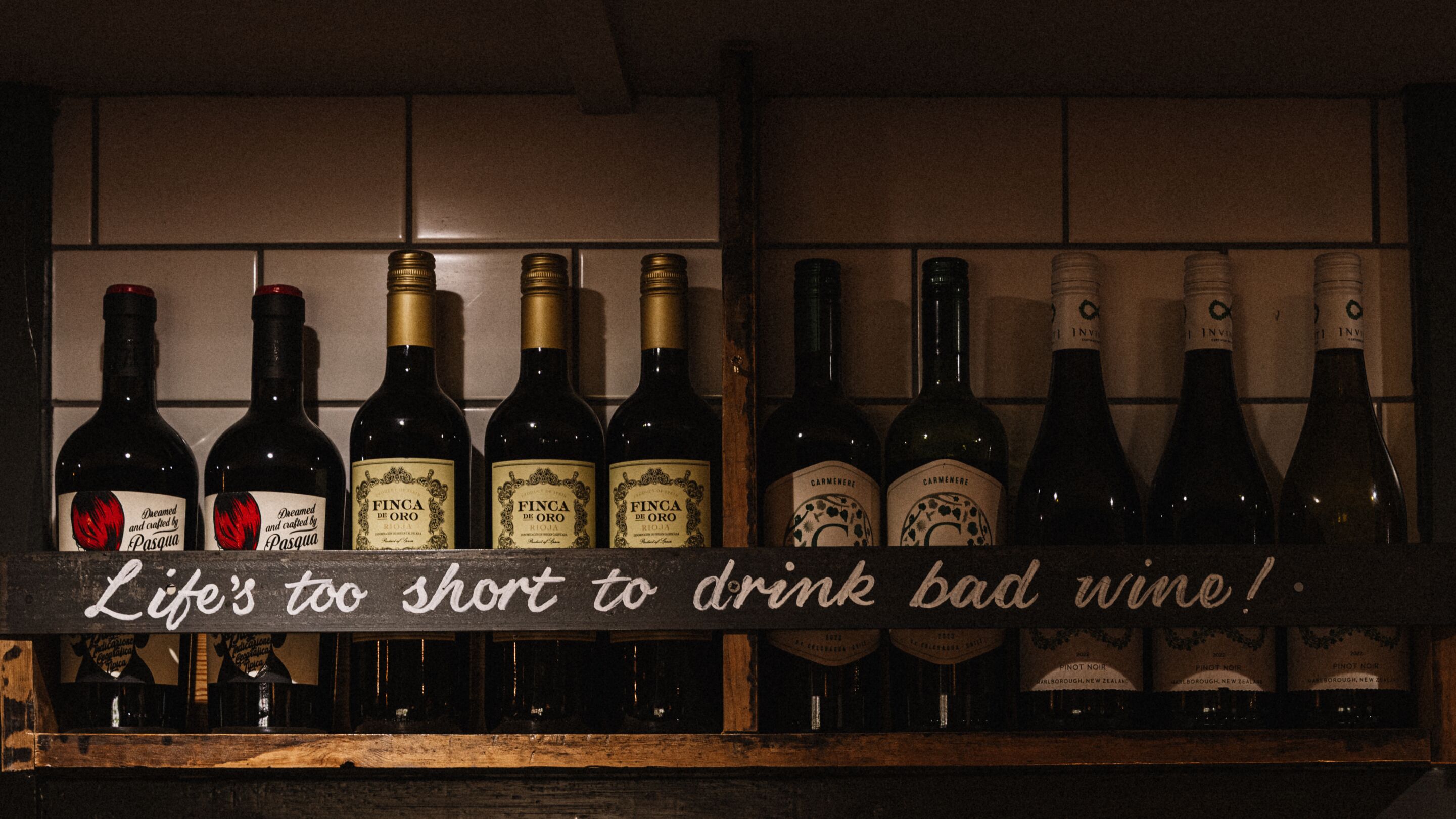 A shelf with various wine bottles and a sign that reads 'Life's too short to drink bad wine!'