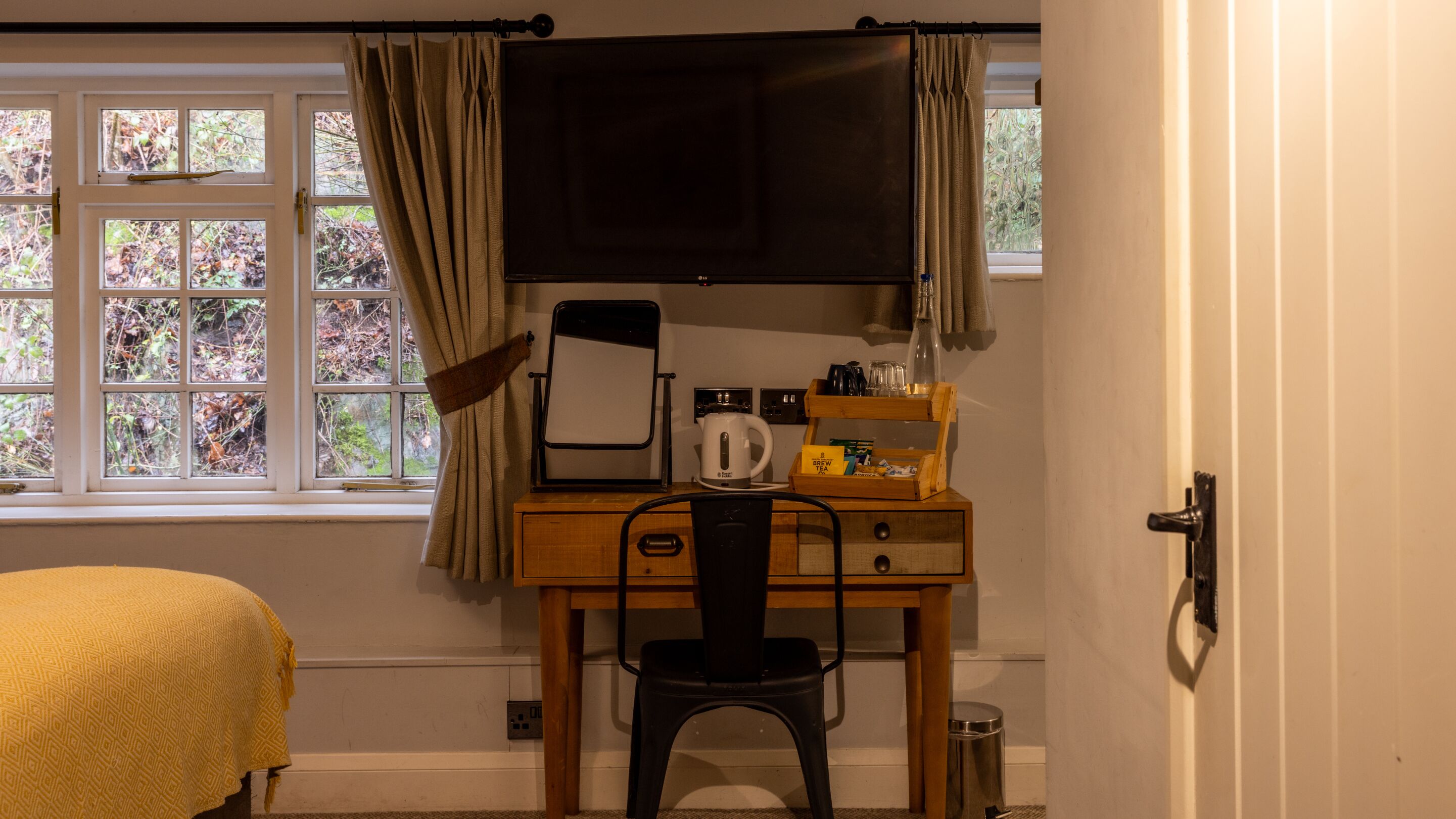 A room with a bed, a desk with a chair, a television, and a window with curtains.