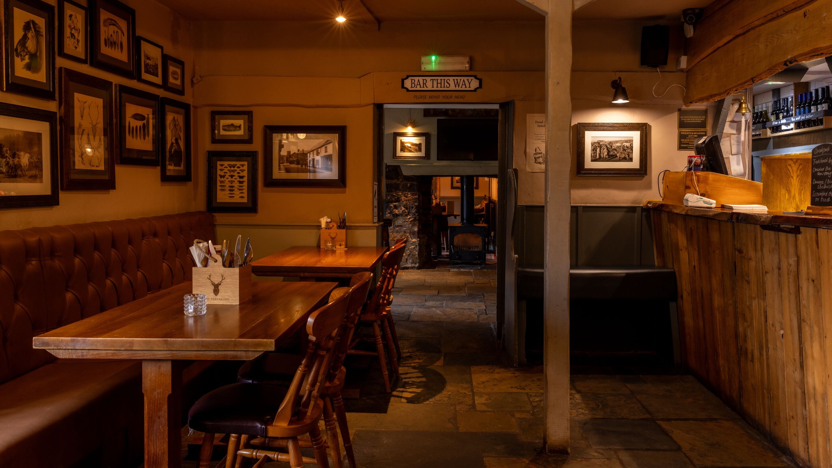 Un rincón acogedor con bar, muebles de madera, cuadros en las paredes y un letrero que dice 'BAR THIS WAY'.