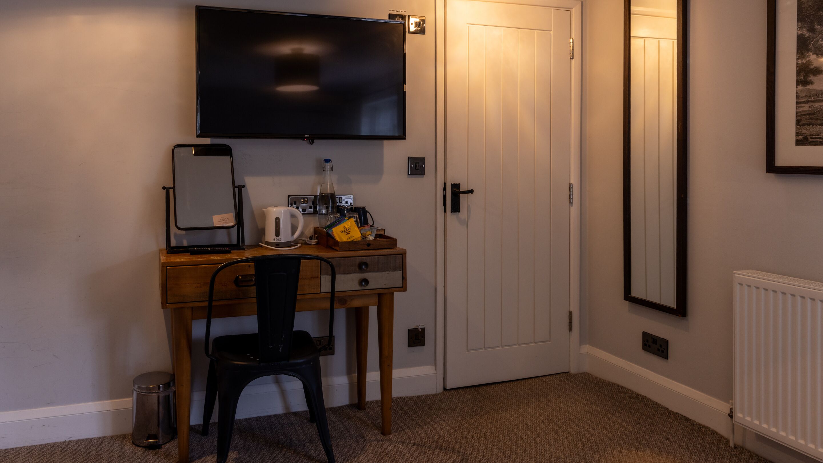 Een hotelkamer met een bureau, stoel, flatscreen televisie en een deur.
