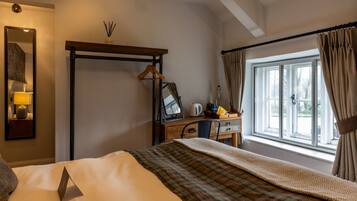 Una habitación de hotel con cama, escritorio con espejo, tetera y ventana con cortinas.